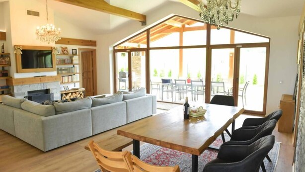 A spacious living area with a wooden dining table, grey sofa, and a chandelier.
