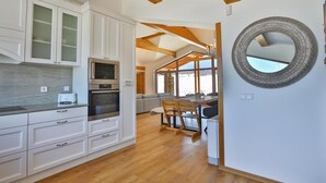 A modern kitchen with white cabinetry, a built-in oven, and a dining area with a wooden table and chairs.