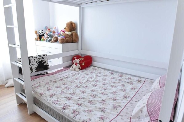 Una cama litera blanca con una colcha estampada con flores y un cojín con forma de corazón.