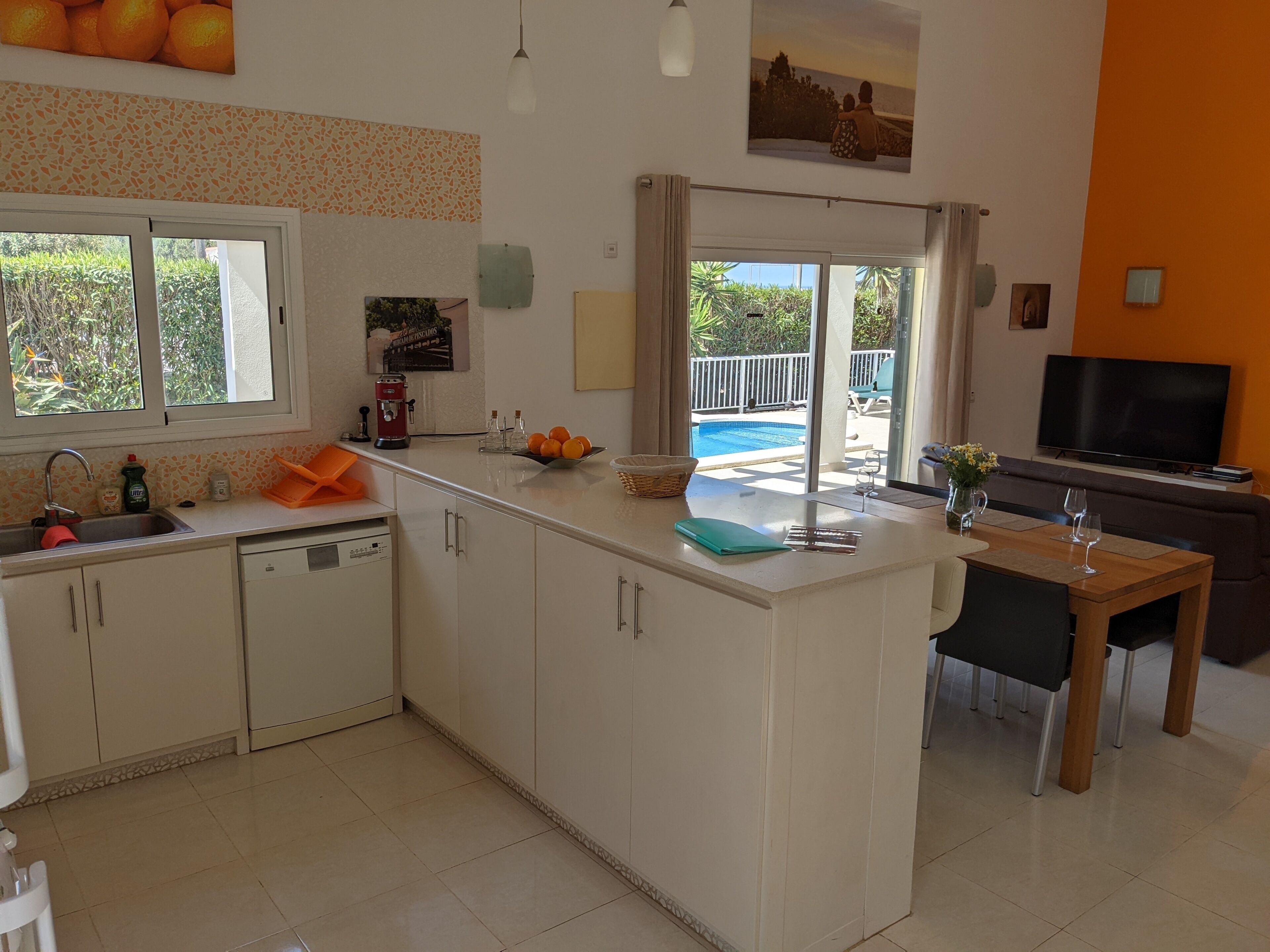 A modern kitchen with a central island, a dining area with a TV, and a view of an outdoor pool.