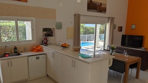 Een moderne keuken met een centraal eiland, een eethoek met televisie en uitzicht op een buitenzwembad.