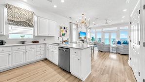 A spacious kitchen with white cabinetry, a central island, and a view to the living area.