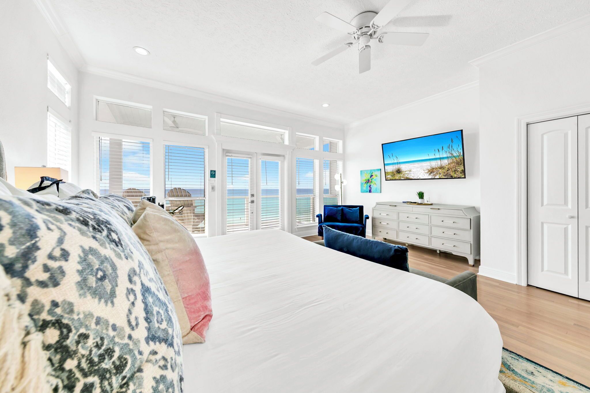 A spacious bedroom with a large bed, a ceiling fan, a dresser, and a painting of a beach scene.