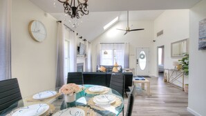 Un coin repas avec une table en verre pour quatre personnes, un lustre et un ventilateur de plafond.