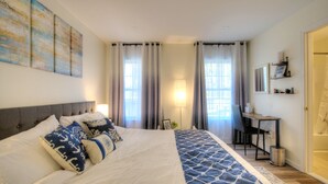 Une chambre bien rangée, avec un grand lit, un bureau, une chaise, ainsi qu’une fenêtre et des rideaux.