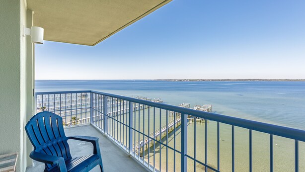 A balcony with a view of the sea, a blue chair, and a white railing.
