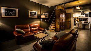 Een moderne woonkamer met leren banken, een salontafel en ingelijste foto’s aan de muur. Een trap leidt naar een verdieping erboven.