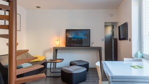 A modern living room with a staircase, a sofa, ottomans, a small table, and a TV mounted on the wall. - LOFT ON THE BANKS OF THE LOIRE (Montlouis-sur-Loire)