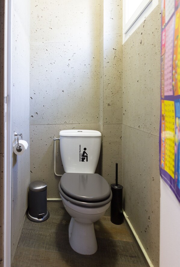 A small, narrow bathroom with a toilet, a trash can, and a toilet brush.