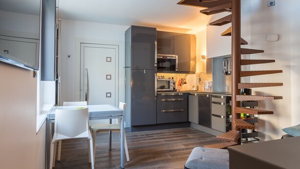 A modern kitchen with grey cabinets, a built-in oven, and a microwave. There is a dining area with a white table and chairs. - LOFT ON THE BANKS OF THE LOIRE (Montlouis-sur-Loire)