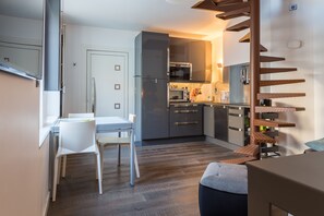 A modern kitchen with grey cabinets, a built-in oven, and a microwave. There is a dining area with a white table and chairs.