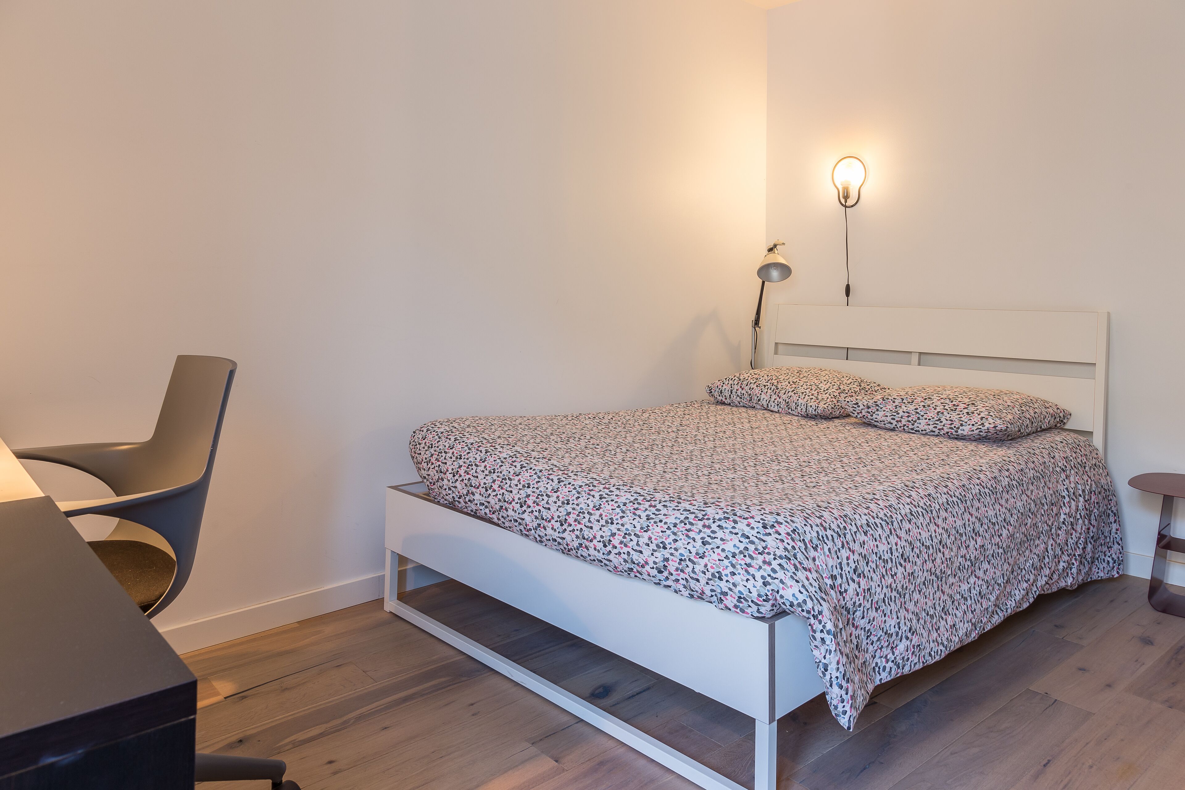 Un dormitorio moderno con una cama blanca, un escritorio y una silla.