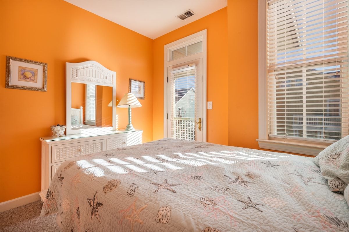 Une chambre à coucher avec un lit, une commode, un miroir et une fenêtre avec des stores.