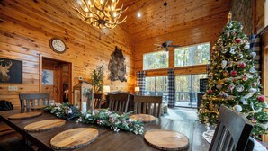 A wooden interior with a Christmas tree, dining table with round wooden boards, and a mounted clock. - Secluded Cabin: Sleeps 10, New Hot Tub, Fire Pit, Arcade, Foosball & Deck Slide (Broken Bow)