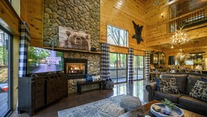 A cozy cabin interior with a stone fireplace, wooden walls, a large television, and a dining area. - Secluded Cabin: Sleeps 10, New Hot Tub, Fire Pit, Arcade, Foosball & Deck Slide (Broken Bow)