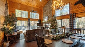 A cozy cabin interior with a wooden dining table set for four, a fireplace, and a Christmas tree. - Secluded Cabin: Sleeps 10, New Hot Tub, Fire Pit, Arcade, Foosball & Deck Slide (Broken Bow)