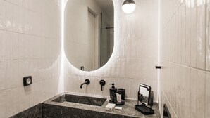 A modern bathroom with a large oval mirror, a rectangular sink with a marble countertop, and a black towel rack.