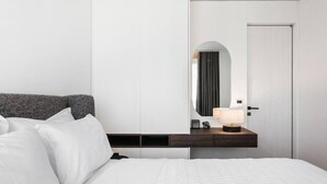 A modern hotel room with a neatly made bed, a dark headboard, a bedside table with a lamp, and a large mirror.