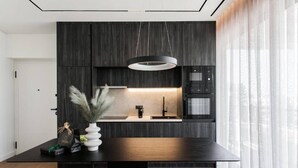 A modern kitchen with dark wood cabinetry, a central island with a black countertop, a hanging pendant light, and a built-in oven.