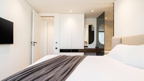 Ein modernes Hotelzimmer mit einem großen Bett, einem flachbildfernseher an der Wand und einem minimalistischen Design.