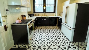 Uma cozinha com piso em padrão preto e branco, fogão a gás, micro-ondas, pia e geladeira.