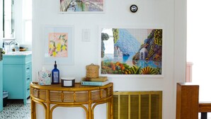 Quarto com piso de madeira, uma mesa de vime com um cesto e uma parede com três obras de arte emolduradas.