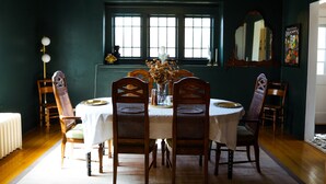 Uma sala de jantar com uma mesa redonda, quatro cadeiras de madeira, um candelabro e uma grande janela com vários painéis.