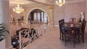 Un comedor con candelabro, barandilla ornamentada y una escalera que sube a un nivel superior.