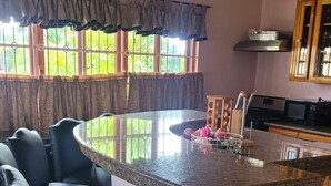 Una cocina con encimera de granito, estufa integrada y microondas. Hay dos taburetes negros y una ventana con cortinas.