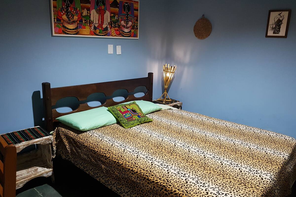 Une chambre à coucher avec une tête de lit en bois, un lit recouvert d’une couvre-lit à motifs léopard, deux oreillers, une table de chevet avec une lampe et une décoration murale.