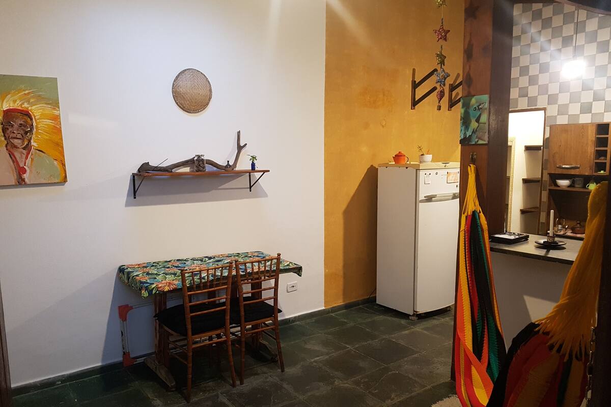 Une cuisine compacte avec un coin repas, comprenant un réfrigérateur blanc, une petite étagère avec des objets décoratifs et une table à manger avec des chaises.