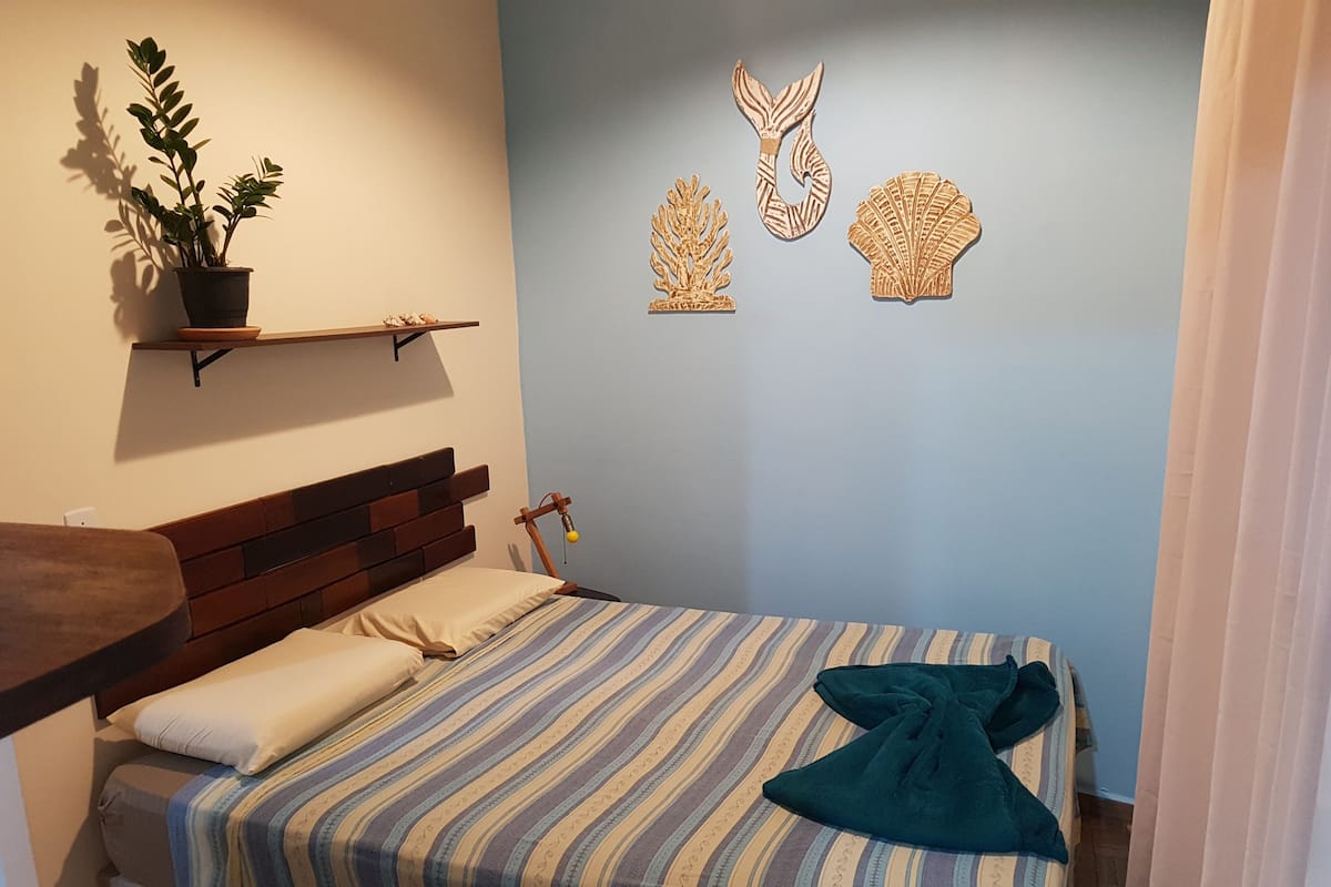 Une chambre à coucher avec un lit, une tête de lit en bois, une table de chevet, une plante en pot et des décorations murales.