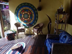 A wooden deck with wicker furniture, a colorful tapestry, and a rustic shelf with various items. - Casa Tribus Itamambuca (Ubatuba)