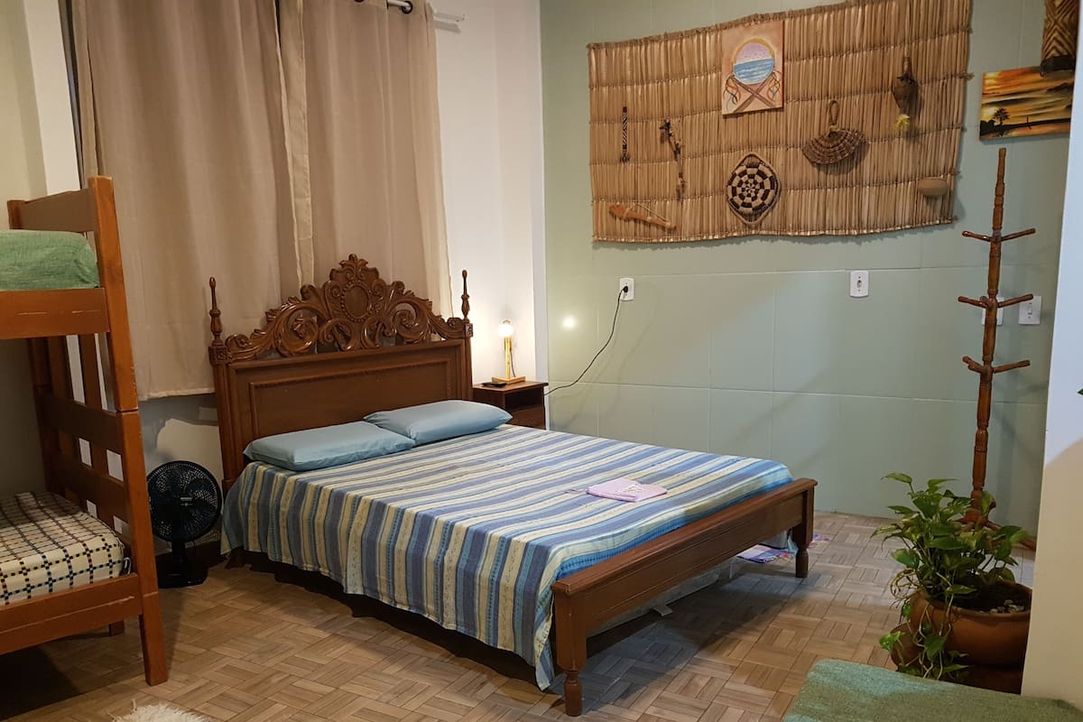 Une chambre avec un lit en bois, un lit superposé, une table de chevet avec une lampe, un mur décoré et une plante en pot.