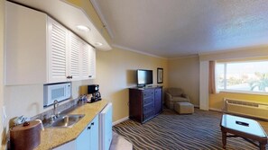 A compact hotel room with a kitchenette, a flat-screen TV, a sofa, and a large window.