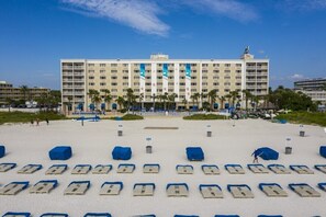 A hotel with a large building, a sandy beach in front, and rows of blue beach chairs.