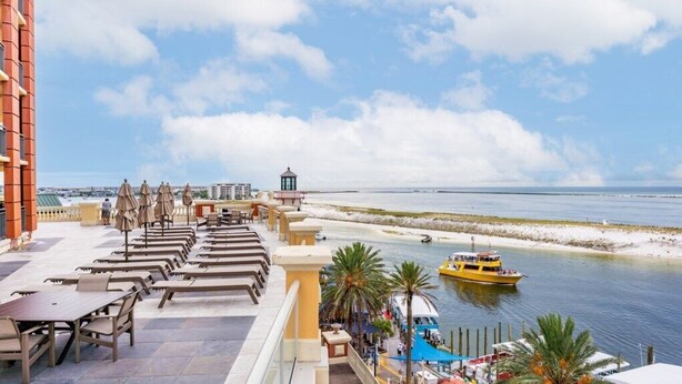 A seaside terrace with outdoor seating, a view of the ocean, and a boat in the water. - Club Wyndham Emerald Grande - 1 Bedroom (Destin)