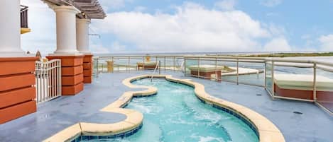 Zona de piscina con diseño serpenteante, rodeada por una barandilla de cristal y vistas al mar.