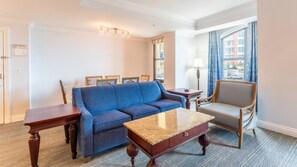 Una sala de estar con un sofá azul, una mesa de centro de madera, una mesita auxiliar de madera y un sillón de madera.