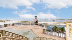 Vista para a praia com um farol, areal arenoso e uma área pavimentada com padrão de estrelas.