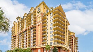Un hôtel à plusieurs étages, doté de balcons, d’une colonne centrale de couleur rouge et surplombant un ciel dégagé.