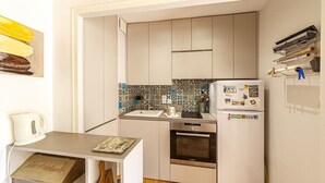 A compact kitchen with white cabinets, a Bosch oven, a refrigerator with magnets, and a tiled backsplash.