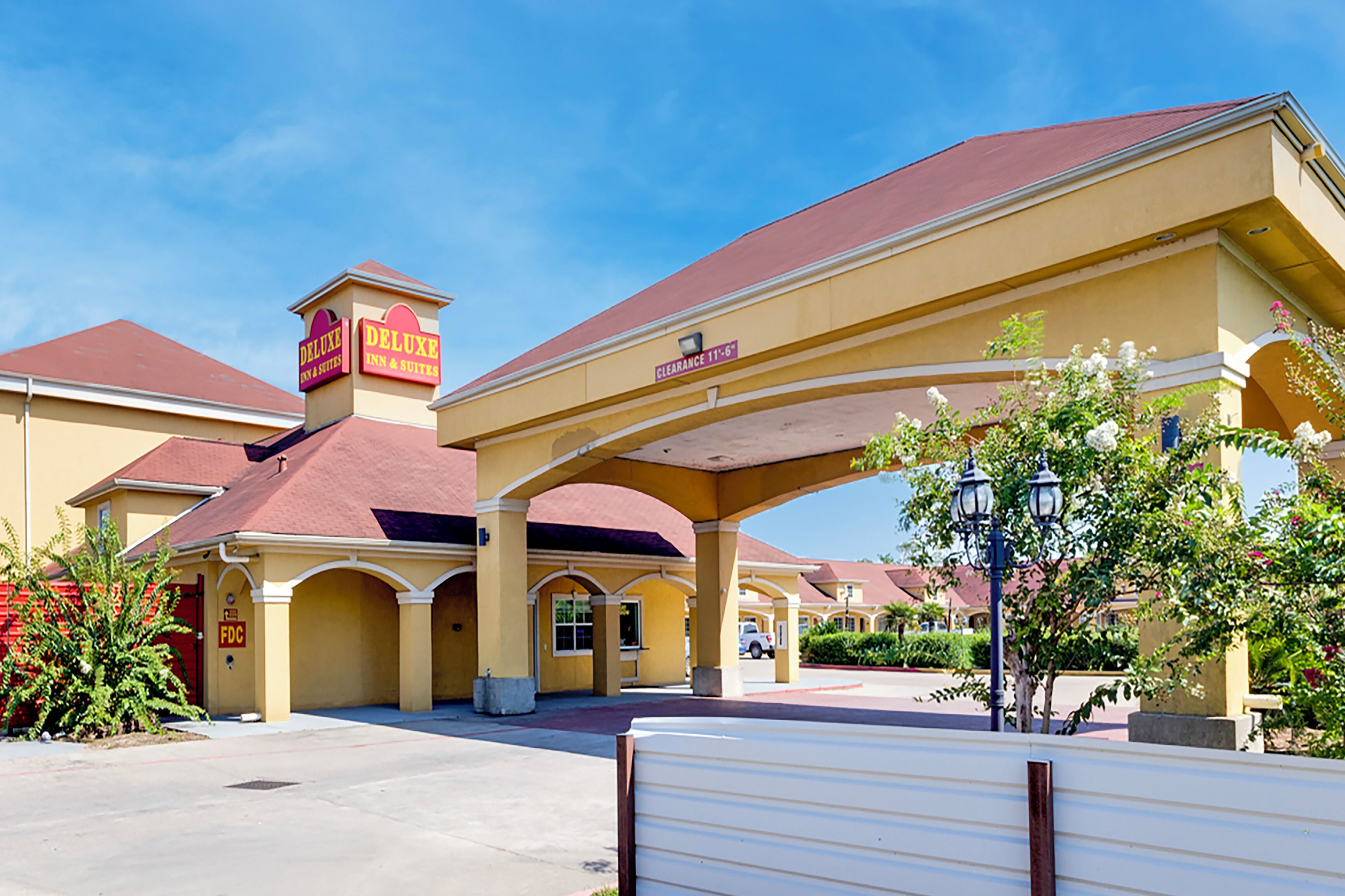 A hotel with a yellow facade, red roof, and a covered parking area.