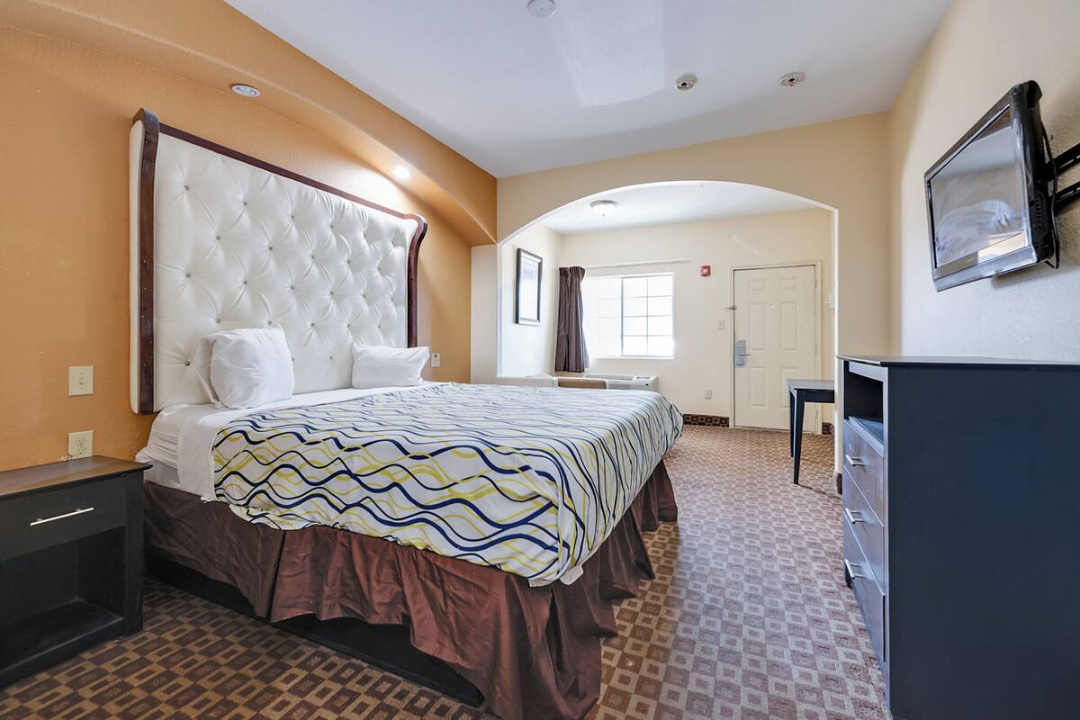 A hotel room with a large bed, a desk, and a dresser.