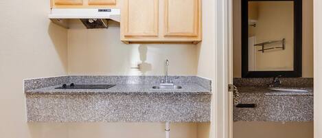A kitchen with granite countertops, a stainless steel sink, wooden cabinets, and a visible electrical outlet.