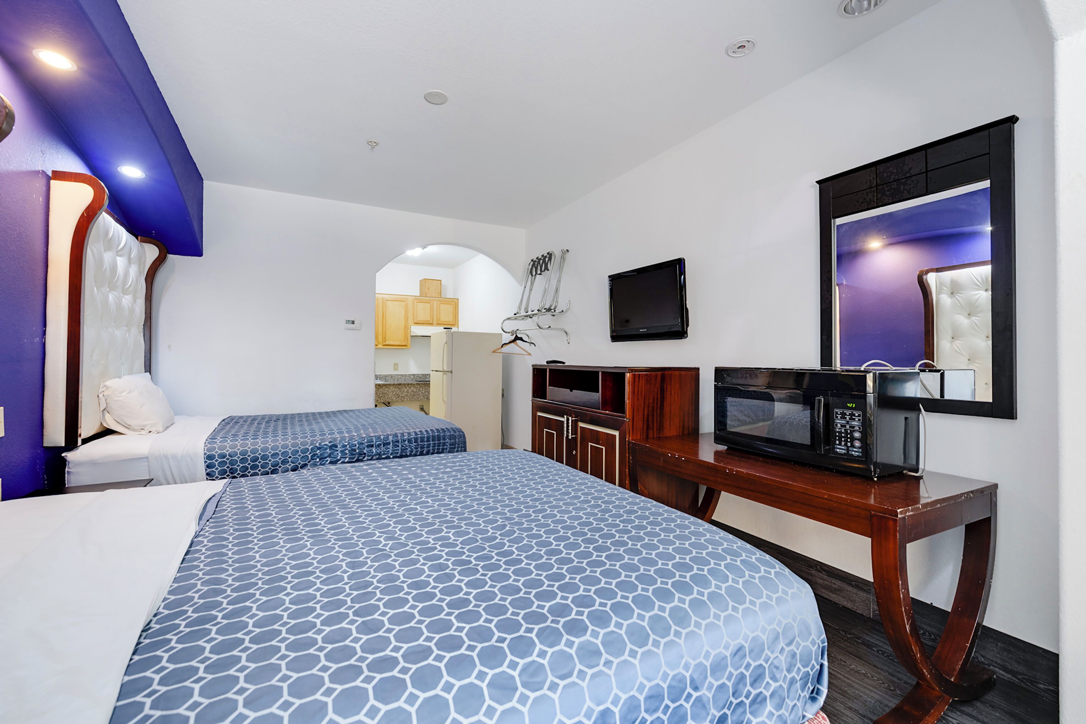 A hotel room with two beds, a desk with a microwave, and a TV on the wall.
