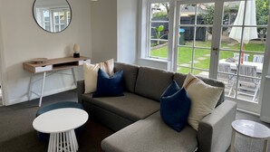 A modern living room with a grey sectional sofa, a round white coffee table, a small white side table, a round mirror, and a hanging paper lantern. - In heart of mission Bay, Pet friendly, minutes walk to the beach (Auckland)