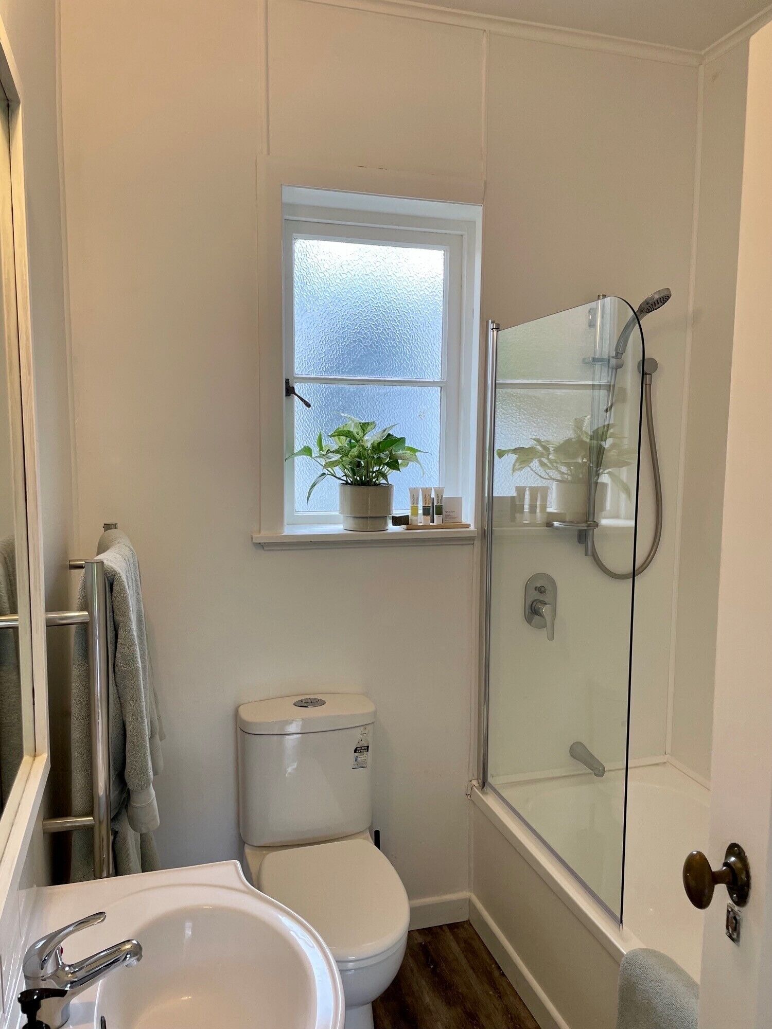 Une petite salle de bain comprenant des toilettes, un lavabo et une douche fermée par une paroi de verre.