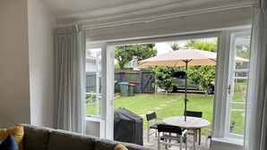 A living room with a grey sofa, a small table, and a patio area with a table and chairs. - In heart of mission Bay, Pet friendly, minutes walk to the beach (Auckland)