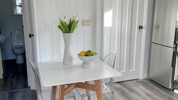 A white dining table with a bowl of fruit and a vase of flowers, set against a white paneled wall.